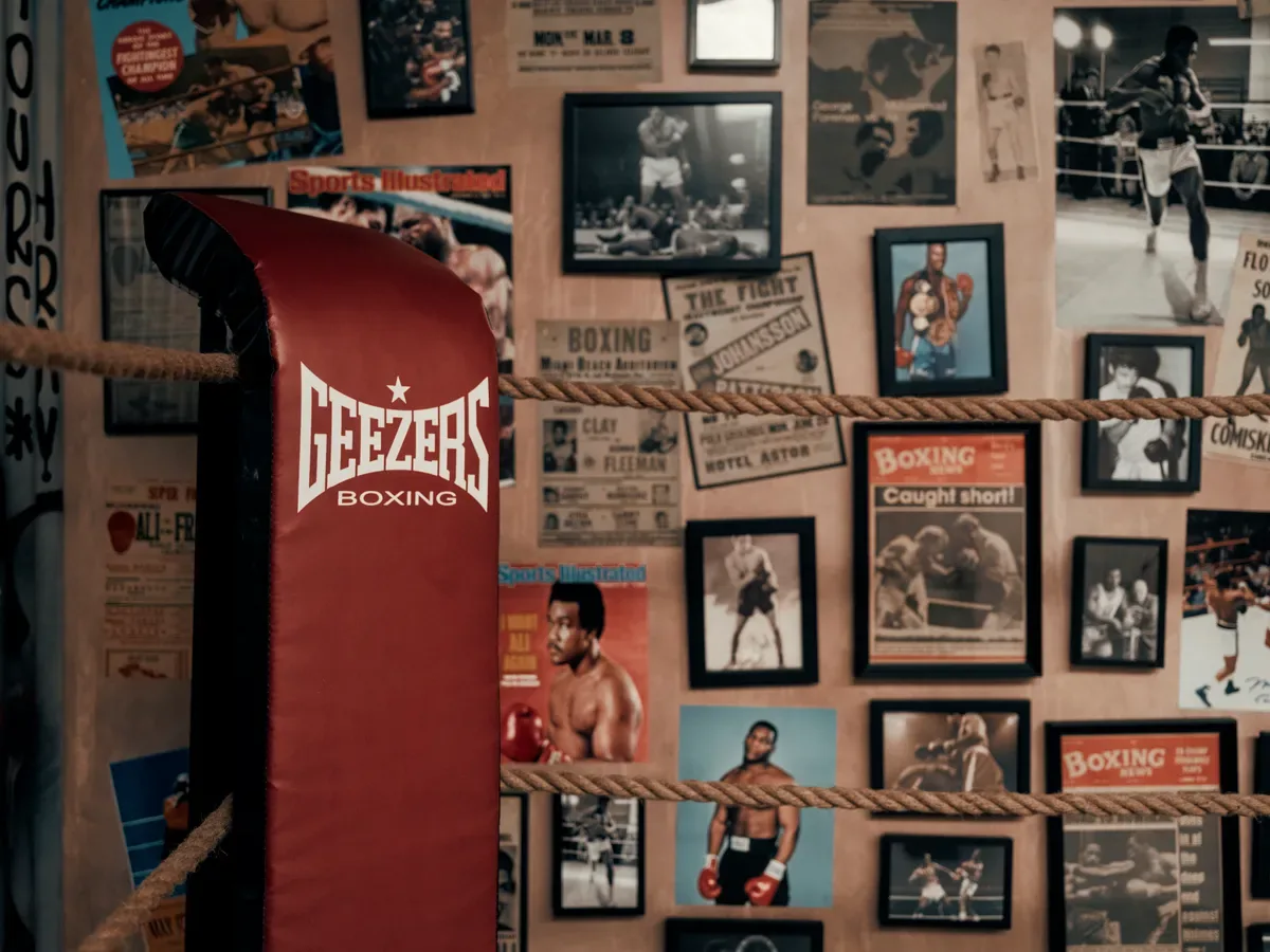 Wall of vintage fight posters and framed photos beside the red heavy bag in The Bowery